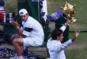WIMBLEDON, ENGLAND - JULY 05:  Andy Roddick of USA looks despondent as Roger Federer of Switzerland celebrates with the trophy during the men's singles final match on Day Thirteen of the Wimbledon Lawn Tennis Championships at the All England Lawn Tennis and Croquet Club on July 5, 2009 in London, England. Federer won 5-7, 7-6, 7-6, 3-6, 16-14.  (Photo by Julian Finney/Getty Images)