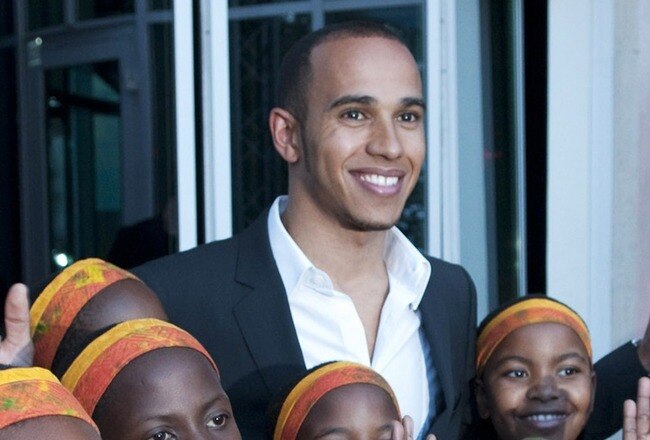 MONTE CARLO, MONACO - MAY 11:  In this handout image provided by Amber Lounge, Lewis Hamilton poses with the African Childrens choir at the Amber Lounge party held at Meridien Beach Plaza on May 15th, 2010 in Monte Carlo, Monaco. (Photo by StillMoving/Getty Images for Amber Lounge)