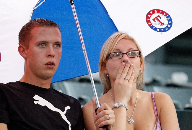 ARLINGTON, TX - SEPTEMBER 11:  As rain falls, fans sit under an umbrella before the start of the Seattle Mariners and the Texas Rangers on September 11, 2009 in Arlington, Texas.  (Photo by Ronald Martinez/Getty Images)
