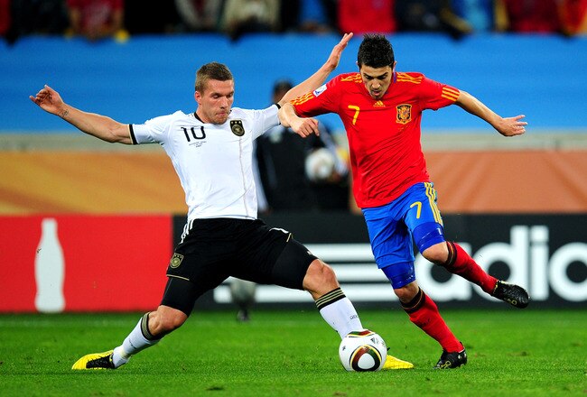 DURBAN, SOUTH AFRICA - JULY 07:  David Villa of Spain is tackled by Lukas Podolski of Germany during the 2010 FIFA World Cup South Africa Semi Final match between Germany and Spain at Durban Stadium on July 7, 2010 in Durban, South Africa.  (Photo by Clive Mason/Getty Images)