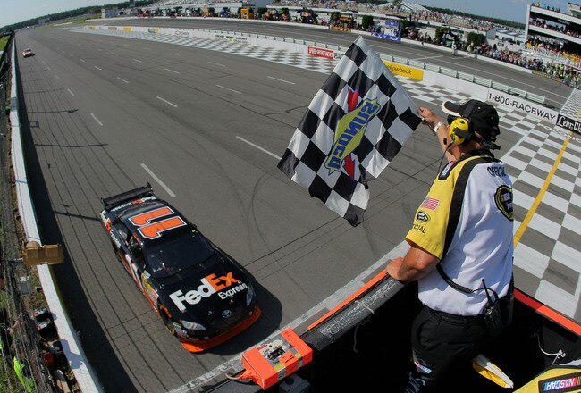 LONG POND, PA - AUGUST 03:  Denny Hamlin, driver of the #11 Federal Express Toyota, comes to the finish line to take the checkered flag from NASCAR flagman Rick Monroe as he took victory in the NASCAR Sprint Cup Series Sunoco Red Cross Pennsylvania 500 at the Pocono Raceway on August 3, 2009 in Long Pond, Pennsylvania.  (Photo by Doug Pensinger/Getty Images)