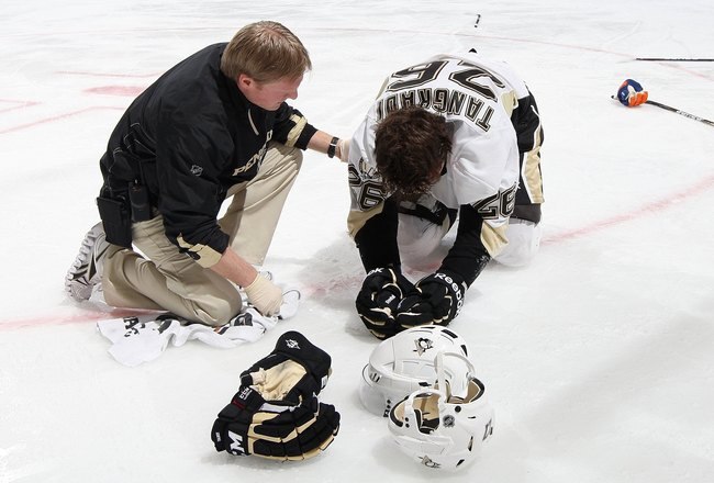 UNIONDALE, NY - FEBRUARY 11:  Eric Tangradi #26 of the Pittsburgh Penguins is tended to by head trainer Chris Stewart after taking a hit to the head from Trevor Gillies (not pictured) of the New York Islanders on February 11, 2011 at Nassau Coliseum in Uniondale, New York. The Isles defeated the Pens 9-3.  (Photo by Jim McIsaac/Getty Images)