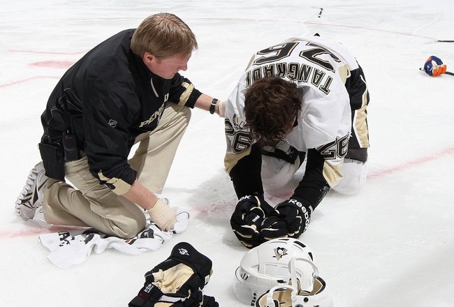 UNIONDALE, NY - FEBRUARY 11:  Eric Tangradi #26 of the Pittsburgh Penguins is tended to by head trainer Chris Stewart after taking a hit to the head from Trevor Gillies (not pictured) of the New York Islanders on February 11, 2011 at Nassau Coliseum in Uniondale, New York. The Isles defeated the Pens 9-3.  (Photo by Jim McIsaac/Getty Images)