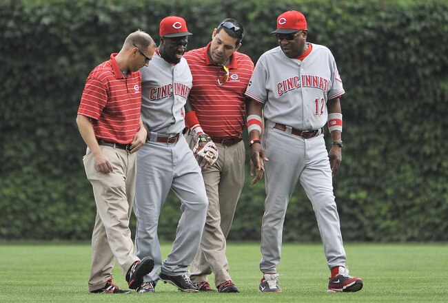 CHICAGO, IL - AUGUST 06:  Manager Dusty Baker #12 (R) of the Cincinnati Reds and trainers help second baseman Brandon Phillips #4 after he collided with right fielder Jay Bruce while going for a pop-up hit by Reed Johnson of the Chicago Cubs during the fourth inning at Wrigley Field on August 6, 2011 in Chicago, Illinois. Phillips stayed in the game and finished the inning, but was taken out in the fifth inning.  (Photo by Brian Kersey/Getty Images)