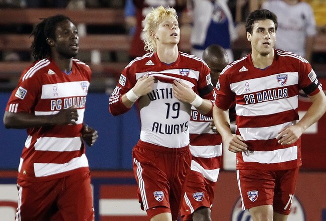 FRISCO, TX - OCTOBER 15: Ugo Ihemelu #3 (L), George John #14 (R) and Brek Shea #20 of the FC Dallas honor former FC Dallas player and broadcaster Bobby Rhine #19 with a undershirt after scoring a goal against Vancouver FC during the second half of a soccer game at Pizza Hut Park on October 15, 2011 in Frisco, Texas. Rhine died suddenly of a heart attack. FC Dallas won 2-0. (Photo by Brandon Wade/Getty Images)