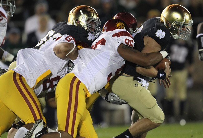 SOUTH BEND, IN - OCTOBER 22: Andrew Hendrix #12 of the Notre Dame Fighting Irish is brought down by Wes Horton #96 and George Uko #90 of the University of Southern California Trojans at Notre Dame Stadium on October 22, 2011 in South Bend, Indiana. (Photo by Jonathan Daniel/Getty Images)