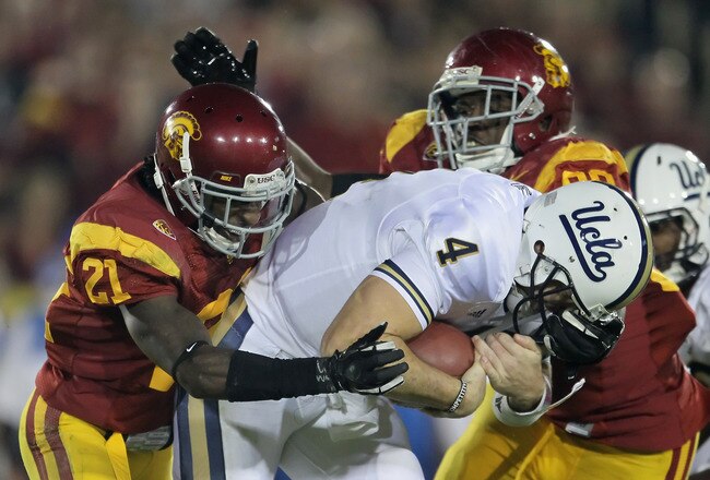 LOS ANGELES, CA - NOVEMBER 26:  Quarterback Kevin Prince #4 of the UCLA Bruins is brought down by Nickell Robey (L) #21 and George Uko #90 of the USC Trojans in the first half at Los Angeles Memorial Coliseum on November 26, 2011 in Los Angeles, California. USC defeated UCLA 50-0.  (Photo by Jeff Gross/Getty Images)