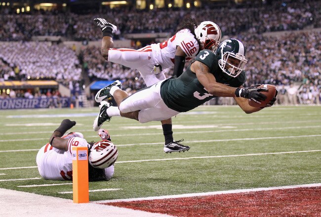 INDIANAPOLIS, IN - DECEMBER 03:  B.J. Cunningham #3 of the Michigan State Spartans runs the ball 6-yards into the endzone after he got the ballo n a lateral by Keith Nichol #7 against Antonio Fenelus #26 and Kevin Claxton #9 of the Wisconsin Badgers during the second quarter of the Big 10 Conference Championship Game at Lucas Oil Stadium on December 3, 2011 in Indianapolis, Indiana.  (Photo by Andy Lyons/Getty Images)