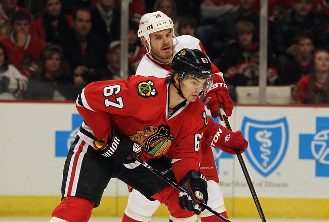 CHICAGO, IL - JANUARY 08:  Michael Frolik #67 of the Chicago Blackhawks passes the puck under pressure from Ian White #18 of the Detroit Red Wings at the United Center on January 8, 2012 in Chicago, Illinois. The Red Wings defeated the Blackhawks 3-2 in overtime.  (Photo by Jonathan Daniel/Getty Images)