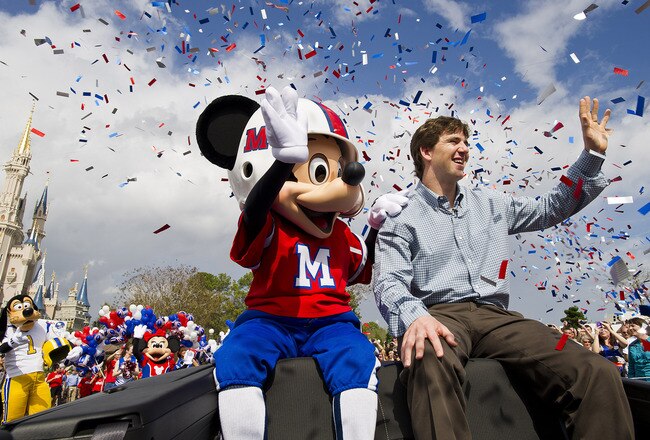 LAKE BUENA VISTA, FL - FEBRUARY 6:   In this handout image provided by Disney Parks, Super Bowl XLVI MVP and New York Giants quarterback Eli Manning takes a celebratory ride with Mickey Mouse on February 6, 2012 at the Magic Kingdom at Walt Disney World Resort in Lake Buena Vista, Florida.  The celebration at the theme park took place only one day after Manning led his team to a 21-17 victory over the New England Patriots in Super Bowl XLVI in Indianapolis.  Immediately following the game, Manning looked into TV cameras and shouted 'I'm Going to Disney World!'  He is the latest star in the famous Disney commercial series. (Photo by Matt Stroshane/Disney Parks via Getty Images)