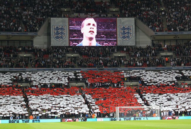 LONDON, ENGLAND - OCTOBER 12: Captain Rio Ferdinand of England is seen on the TV screen as England fans show their support during the national anthem during the UEFA EURO 2012 Group G Qualifying match between England and Montenegro at Wembley Stadium on O