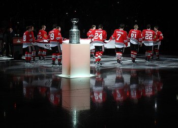 CHICAGO - OCTOBER 09: Members of the Chicago Blackhawks carry the Stanley Cup Championship banner across the ice past the Stanley Cup in a ceremony before the Blackhawks season home opening game against the Detroit Red Wings at the United Center on Octobe