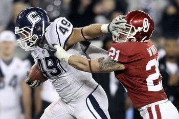 GLENDALE, AZ - JANUARY 01:  Anthony Sherman #49 of the Connecticut Huskies stiff arms Tom Wort #21 of the Oklahoma Sooners in the fourth quarter during the Tostitos Fiesta Bowl at the Universtity of Phoenix Stadium on January 1, 2011 in Glendale, Arizona.