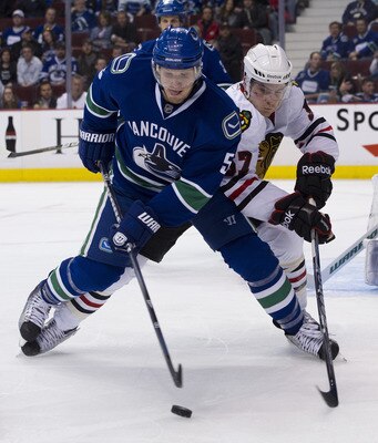 VANCOUVER, CANADA - APRIL 21: Christian Ehrhoff #5 of the Vancouver Canucks tries to clear the puck before getting checked by Ben Smith #57 of the Chicago Blackhawks during the third period in Game Five of the Western Conference Quarterfinals during the 2