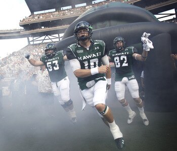 HONOLULU - SEPTEMBER 02: Levi Legay #53, Shane Austin #10, and Jett Jasper #82 of the University of Hawaii Warriors and other team members rush out of the tunnel to take the field in their season opener against the University of Southern California Trojan
