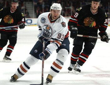 CHICAGO - MARCH 7:  Center Petr Nedved #93 of the Edmonton Oilers pushes the puck between defenders Tyler Arnason #39 and Bryan Berard #4 of the Chicago Blackhawks during a game on March 7, 2004 at the United Center in Chicago, Illinois. The Oilers defeat