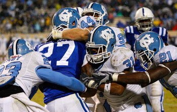 DURHAM, NC - NOVEMBER 29:  Running back Jay Hollingsworth #27 of the Duke Blue Devils is gang-tackled by Jordan Hemby #23, Chase Rice #44, Trimane Goddard #31 and Da'Norris Searcy #21 of the North Carolina Tar Heels during the game at Wallace Wade Stadium