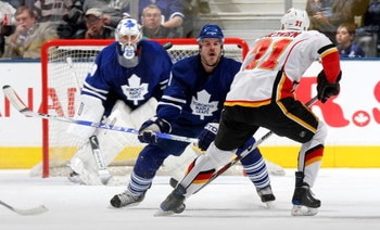 TORONTO - MARCH 14:  Olli Jokinen #21of the Calgary Flames flips the puck past Ian White #7 of the Toronto Maple Leafs as Martin Gerber #29 of the Toronto Maple Leafs looks on during their NHL game at the Air Canada Centre March 14, 2009 in Toronto, Ontar