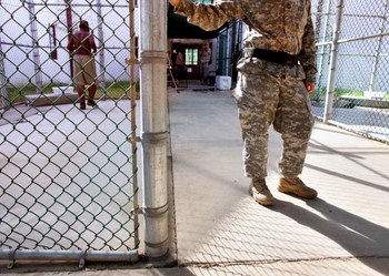 GUANTANAMO BAY, CUBA - JANUARY 20: (NOTE TO EDITORS: PHOTO HAS BEEN REVIEWED BY US MILITARY OFFICIALS) In this photo, reviewed by the U.S. Military, a guard leans on a fencepost as a Guantanamo detainee, left, jogs inside the exercise yard at Camp 5 det