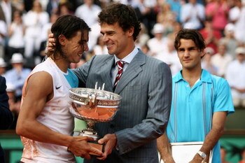 PARIS - JUNE 10:  Rafael Nadal (L) of Spain smiles as he holds the Philippe Chatrier Trophy after winning against Roger Federer (R) of Switzerland with former winner Gustavo Kuerten (C) after the Men's Singles Final on day fifteen of the French Open at Ro