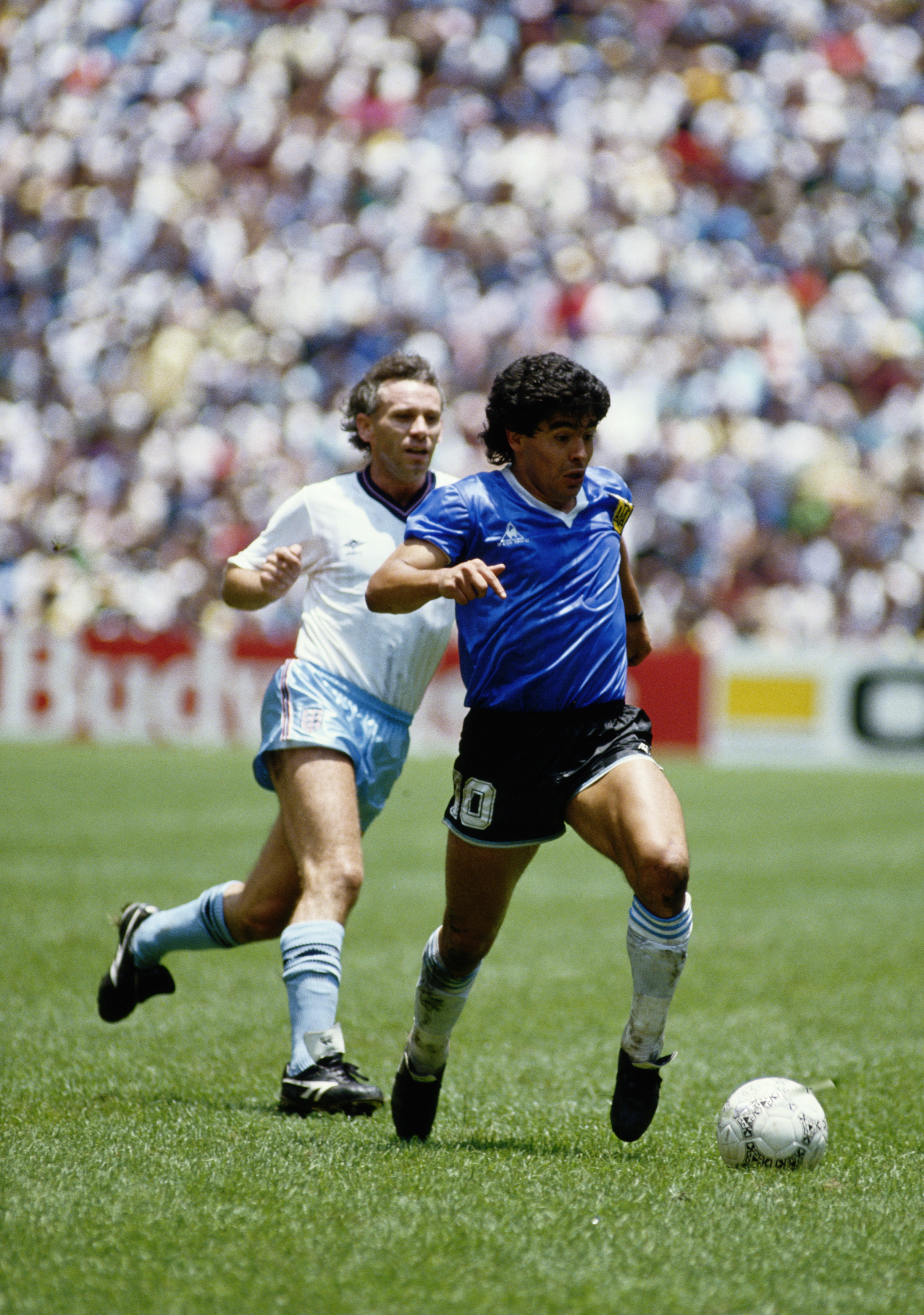 Diego Maradona of Argentina runs with the ball passed Peter Reid of England during the 1986 FIFA World Cup Quarter Final on 22 June 1986 at the Azteca Stadium in Mexico City, Mexico. Argentina defeated England 2-1 in the infamous Hand of God game. (Photo
