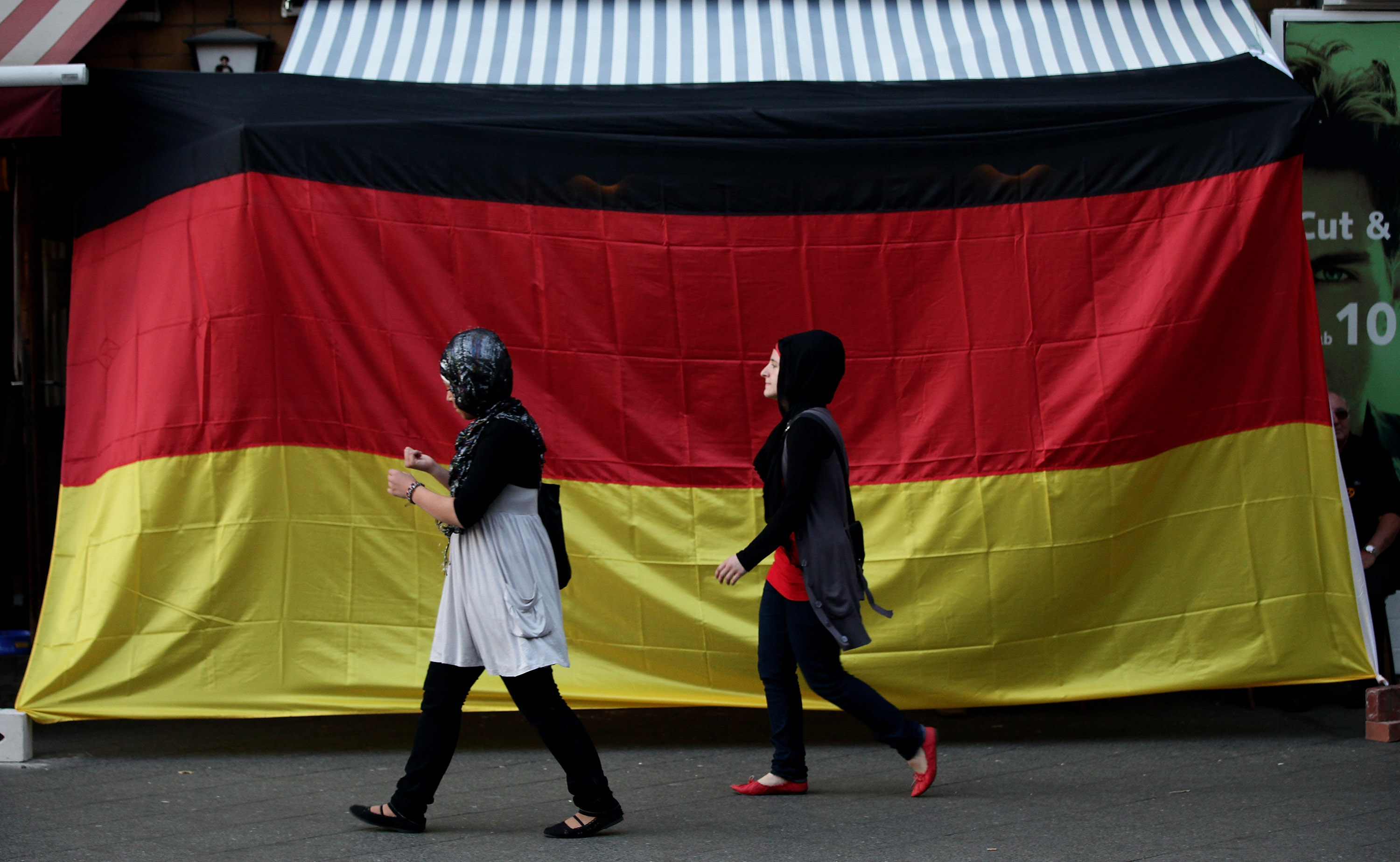 BERLIN - JULY 07:  Two young Muslim women walk by a pub draped in a German flag in the Arab and Turkish-heavy neighborhood of Neukoelln during the FIFA 2010 World Cup match between Germany and Spain on July 7, 2010 in Berlin, Germany. Many immigrants in G