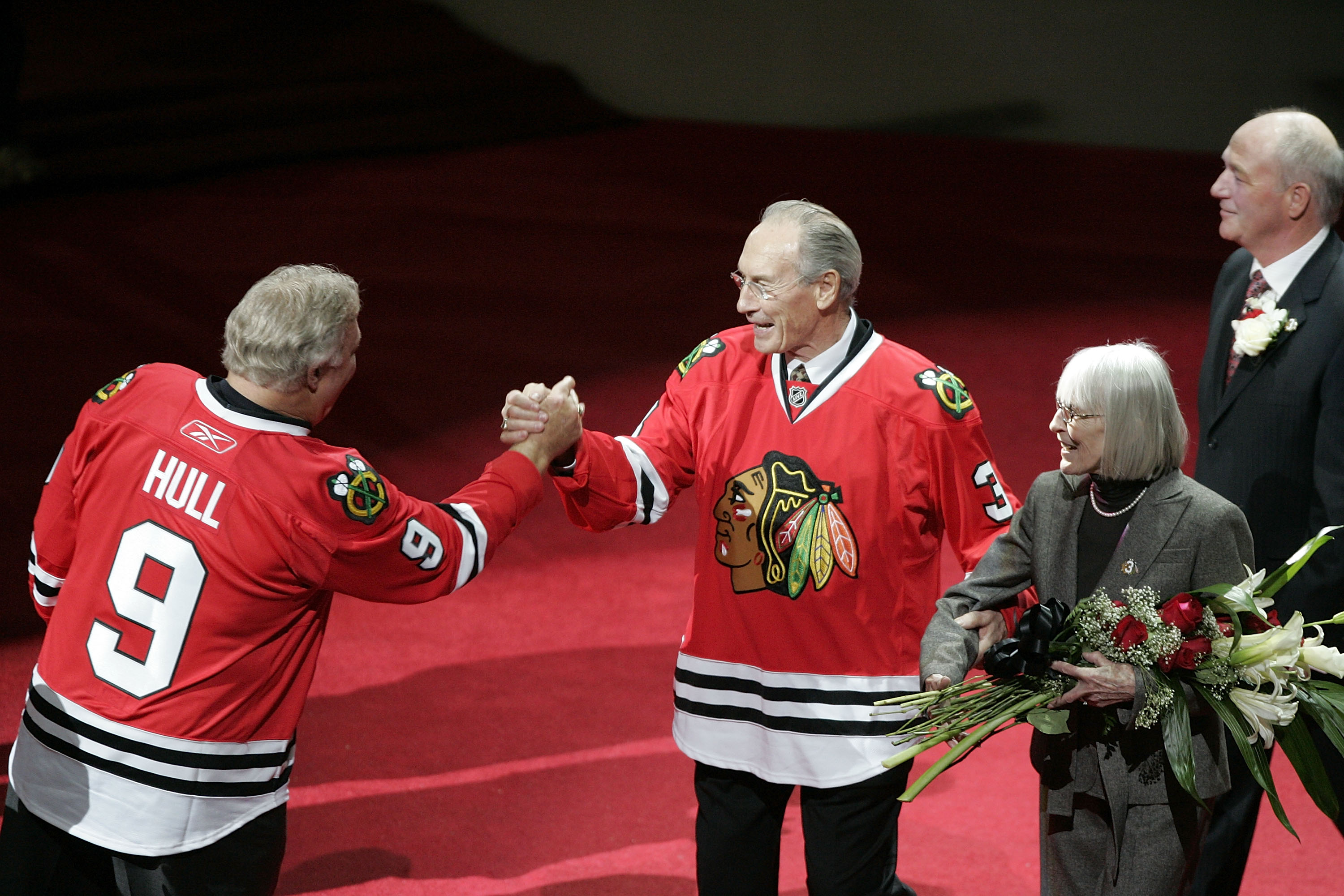 CHICAGO - NOVEMBER 12:  Former Chicago Blackhawks winger and NHL hall of famer Bobby Hull (L) shakes hands with fellow hall of famer and former Blackhawks defenseman Pierre Pilote (C), with his wife Anne, during a ceremony retiring Pilote and Keith Magnus