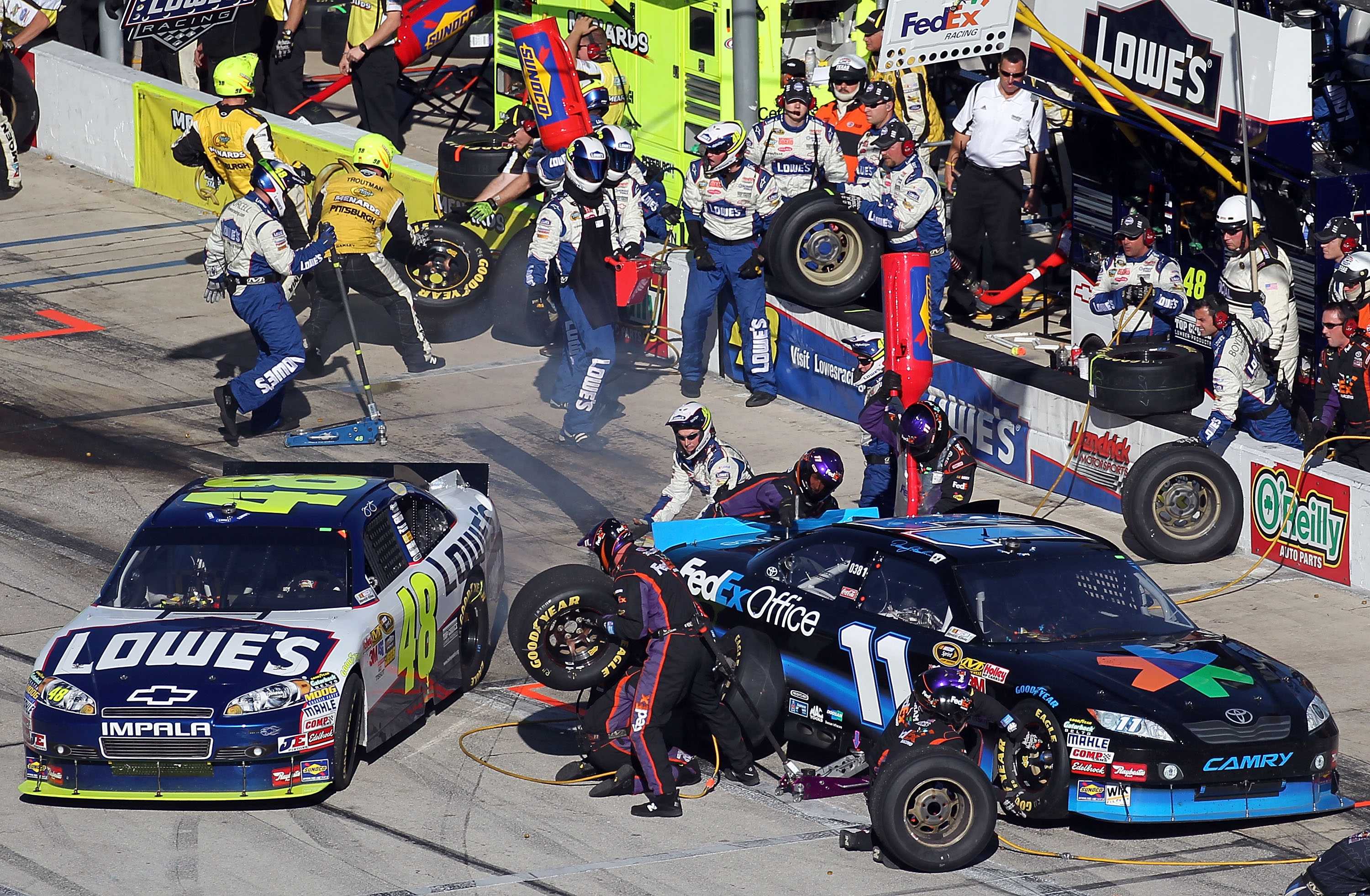 FORT WORTH, TX - NOVEMBER 07:  Jimmie Johnson, driver of the #48 Lowe's Chevrolet, pulls out of his pit as Denny Hamlin, driver of the #11 FedEx Office Toyota, makes a pit stop during the NASCAR Sprint Cup Series AAA Texas 500 at Texas Motor Speedway on N