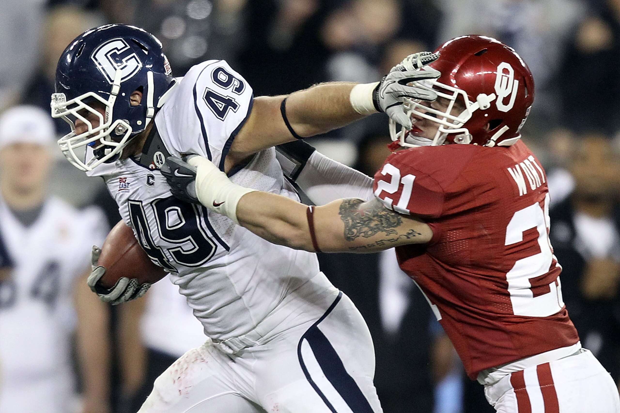 GLENDALE, AZ - JANUARY 01:  Anthony Sherman #49 of the Connecticut Huskies stiff arms Tom Wort #21 of the Oklahoma Sooners in the fourth quarter during the Tostitos Fiesta Bowl at the Universtity of Phoenix Stadium on January 1, 2011 in Glendale, Arizona.