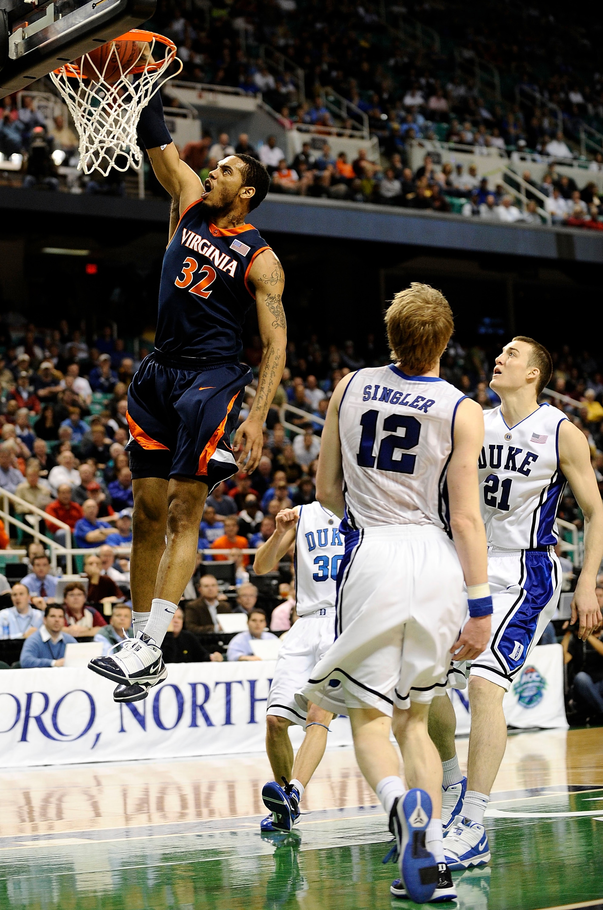 GREENSBORO, NC - MARCH 12:  Mike Scott #32 of the University of Virginia Cavaliers drives by Miles Plumlee #21 and Kyle Singler #12  of the Duke Blue Devils guards in their quarterfinal game in the 2010 ACC Men's Basketball Tournament at the Greensboro Co