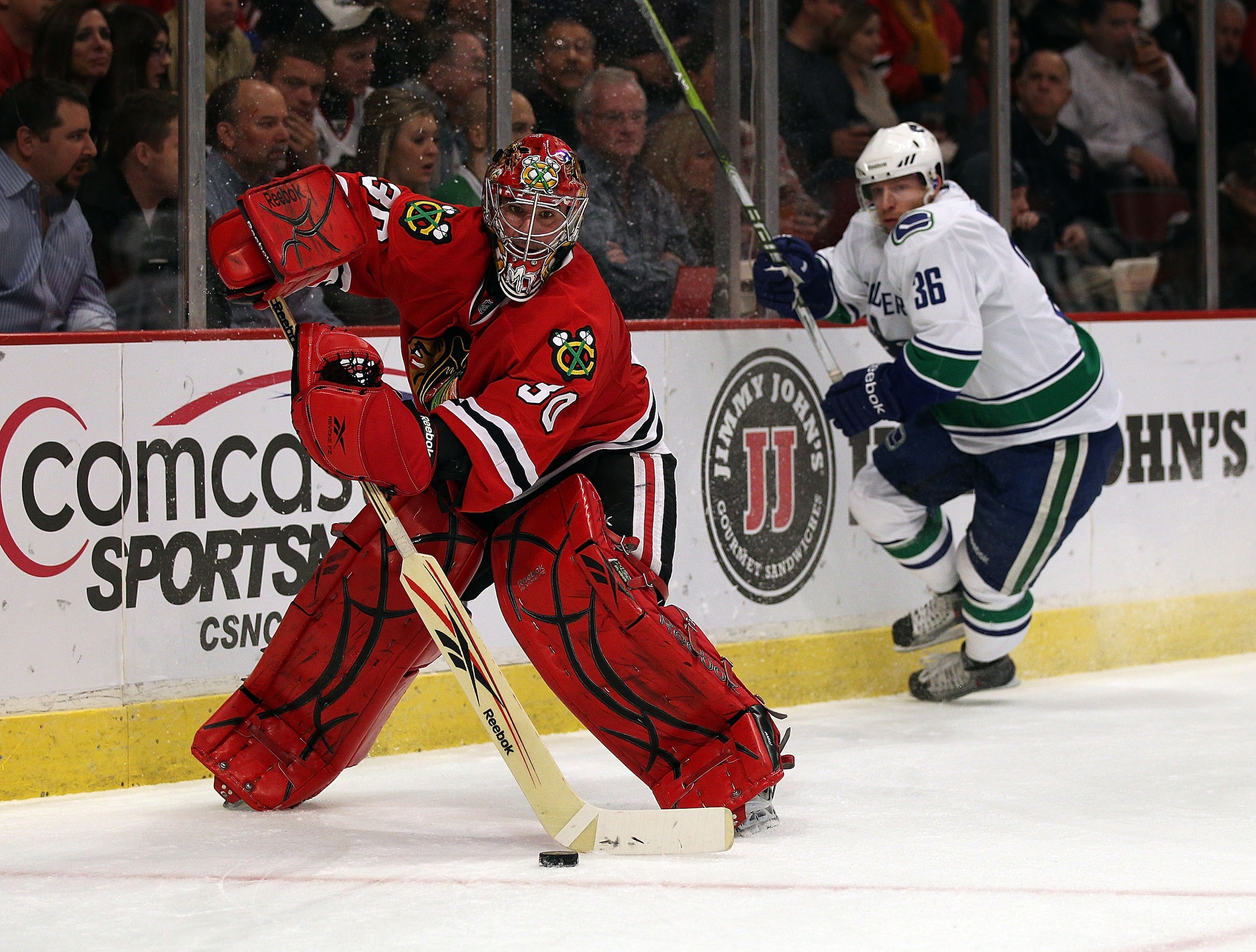 CHICAGO, IL - DECEMBER 03: Marty Turco #30 of the Chicago Blackhawks skates behind the net to clear the puck as Jannik Hansen #36 of the Vancouver Canucks closes in at the United Center on December 3, 2010 in Chicago, Illinois. The Canucks defeated the Bl