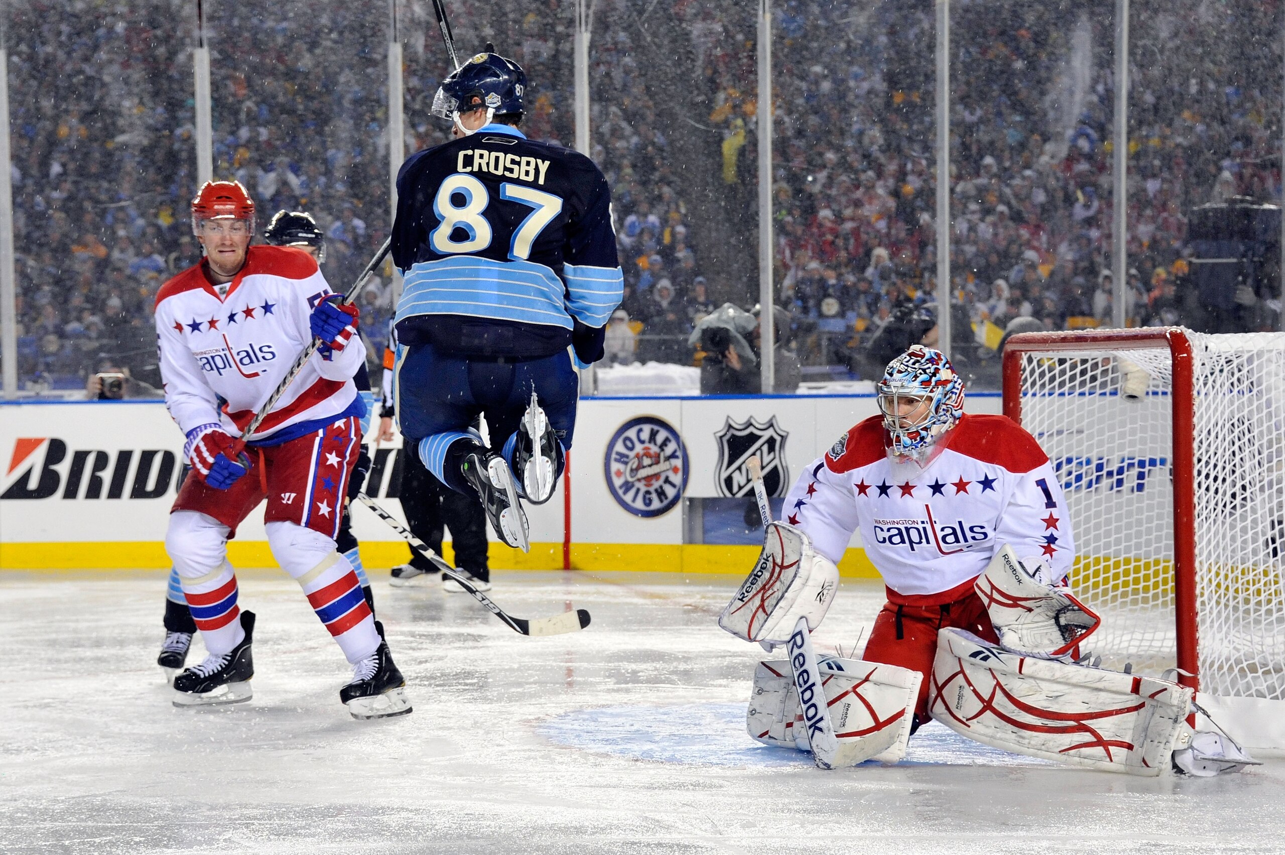 PITTSBURGH, PA - JANUARY 01:  Sidney Crosby #87 of the Pittsburgh Penguins jumps to get out of the way as Semyon Varlamov #1 of the Washington Capitals defends the net during the 2011 NHL Bridgestone Winter Classic at Heinz Field on January 1, 2011 in Pit