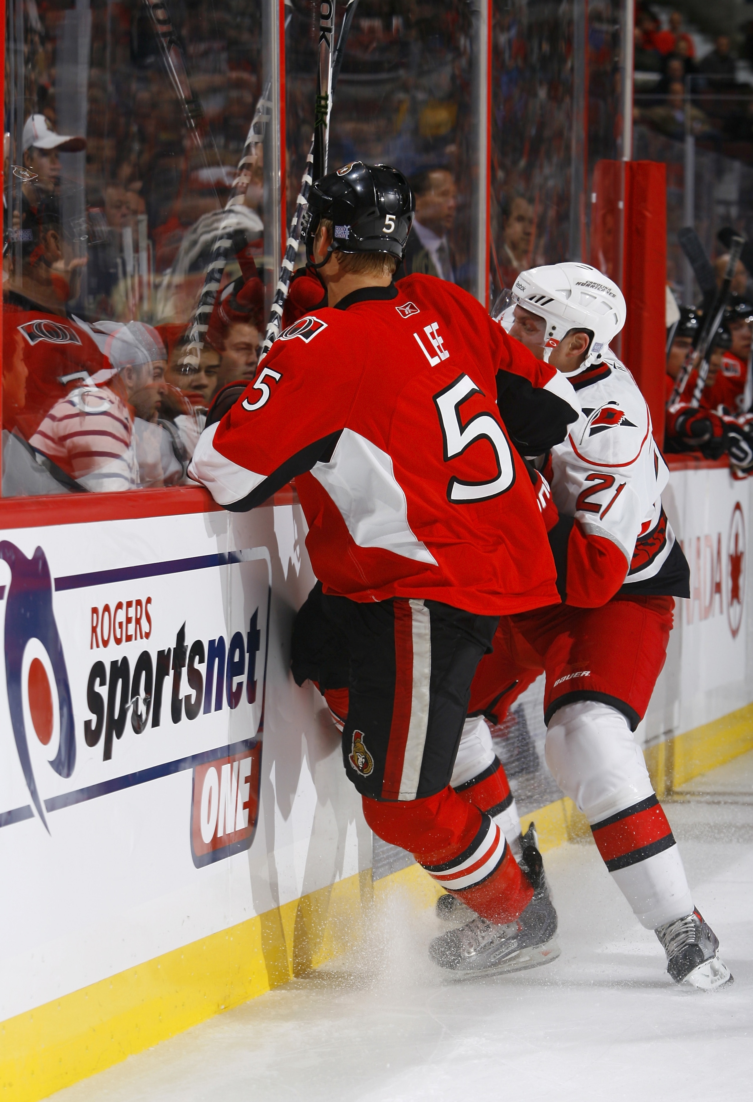 OTTAWA, ON - OCTOBER 14:  Brian Lee #5 of the Ottawa Senators takes a big hit from Drayson Bowman #21 of the Carolina Hurricanes along the near boards during a game at Scotiabank Place on October 14, 2010 in Ottawa, Ontario, Canada.  The Ottawa Senators d