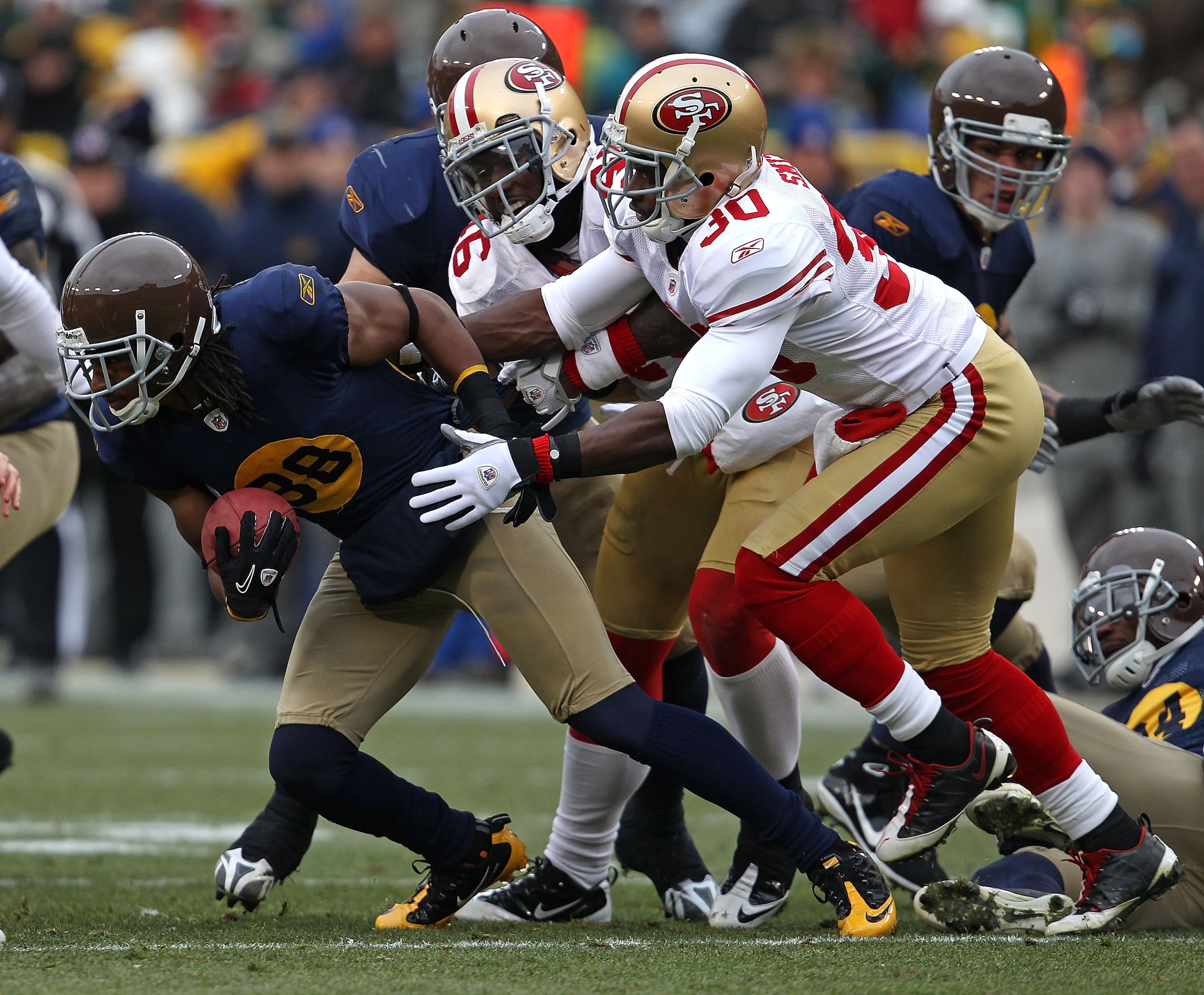 GREEN BAY, WI - DECEMBER 05: Tramon Williams #38 of the Green Bay Packers tries to break away from Delanie Walker #46 and Reggie Smith #30 of the San Francisco 49ers on a punt return at Lambeau Field on December 5, 2010 in Green Bay, Wisconsin. The Packer