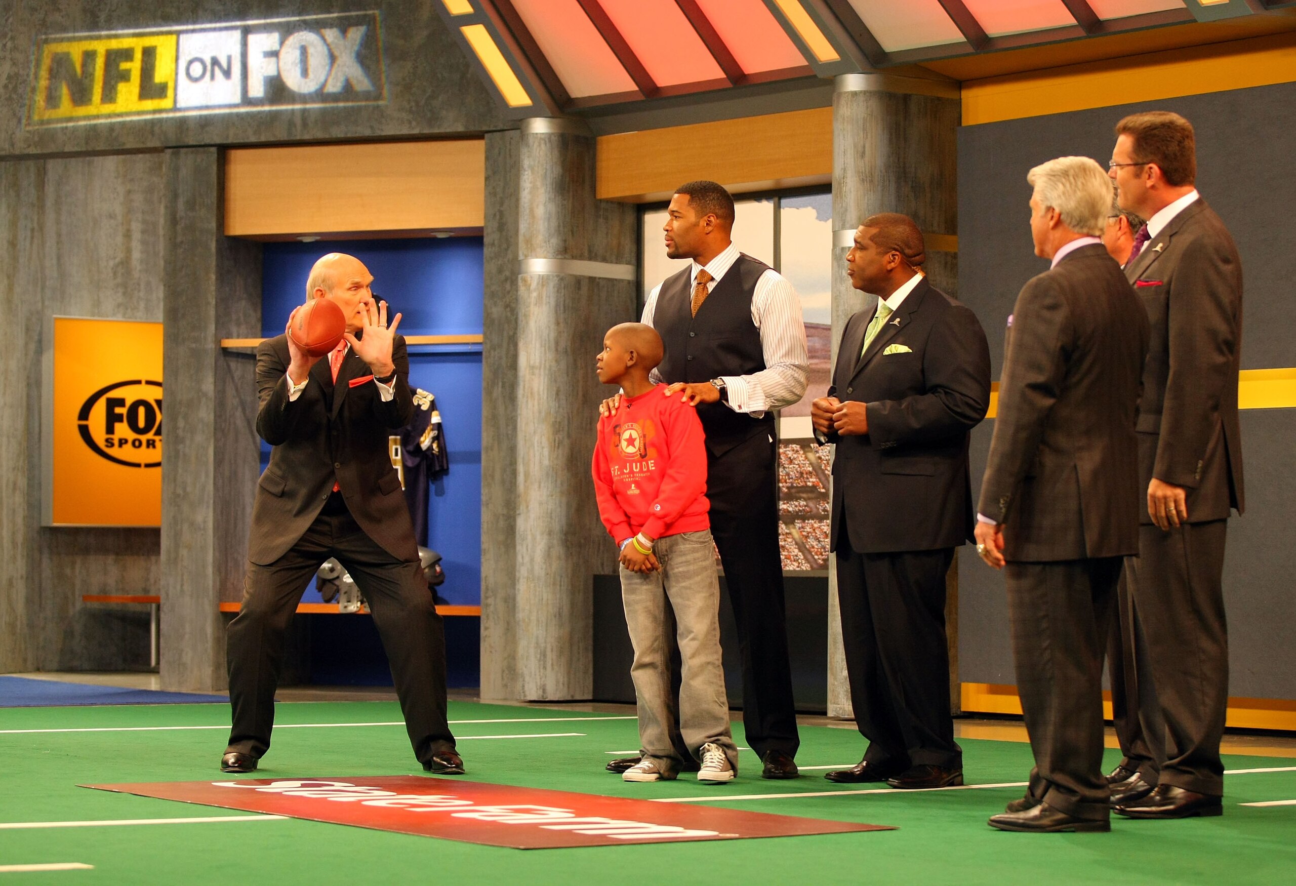 LOS ANGELES, CA - DECEMBER 12: (L-R) FOX NFL Sunday host Terry Bradshaw demonstrates a move to St. Jude Children's Research Hospital patient Markell, analyst Michael Strahan, host Curt Menefee, analysts Jimmy Johnson and Howie Long and former NFL referee LOS ANGELES, CA - DECEMBER 12: (L-R) FOX NFL Sunday host Terry Bradshaw demonstrates a move to St. Jude Children's Research Hospital patient Markell, analyst Michael Strahan, host Curt Menefee, analysts Jimmy Johnson and Howie Long and former NFL referee