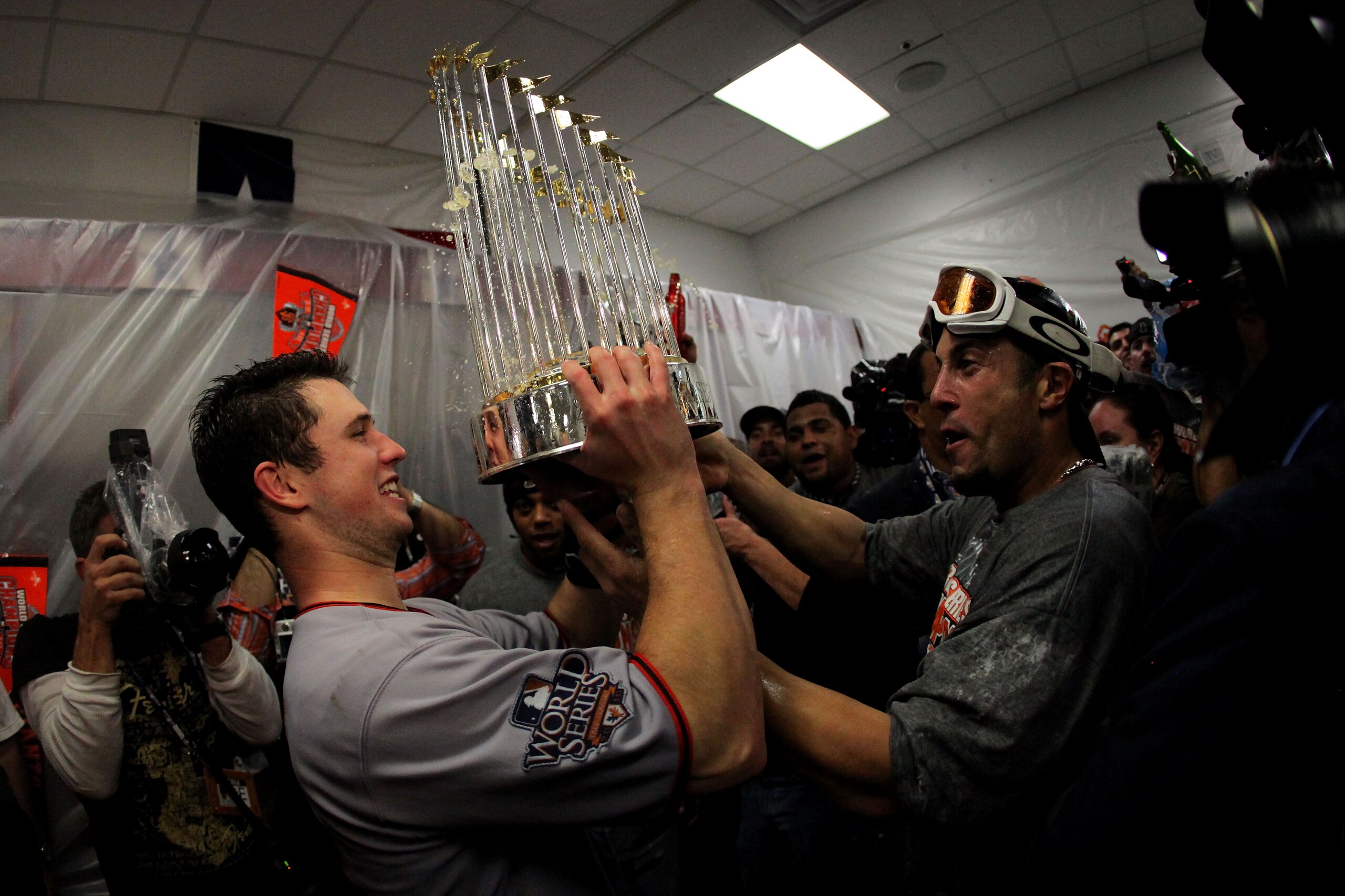 ARLINGTON, TX - NOVEMBER 01:  (L-R) Buster Posey #28 and Andres Torres of the San Francisco Giants celebrates with the trophy in the locker room after the Giants won 3-1 against the Texas Rangers in Game Five of the 2010 MLB World Series at Rangers Ballpa
