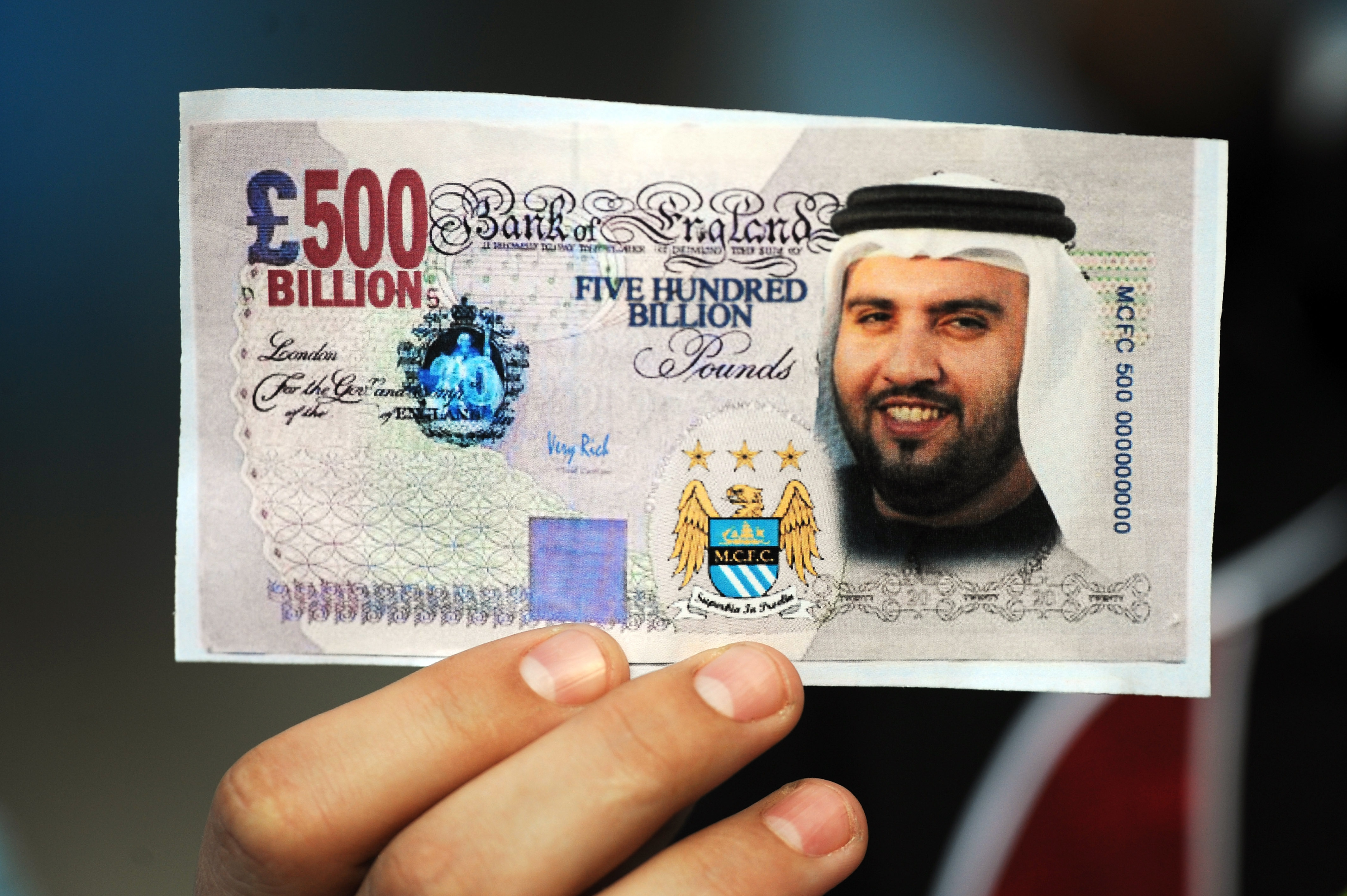 MANCHESTER, UNITED KINGDOM - SEPTEMBER 13:  A Manchester City fan holds a fake British Pound note with the face of Dr Sulaiman Al Fahim during the Barclays Premier League match between Manchester City and Chelsea at The City of Manchester Stadium on Septe
