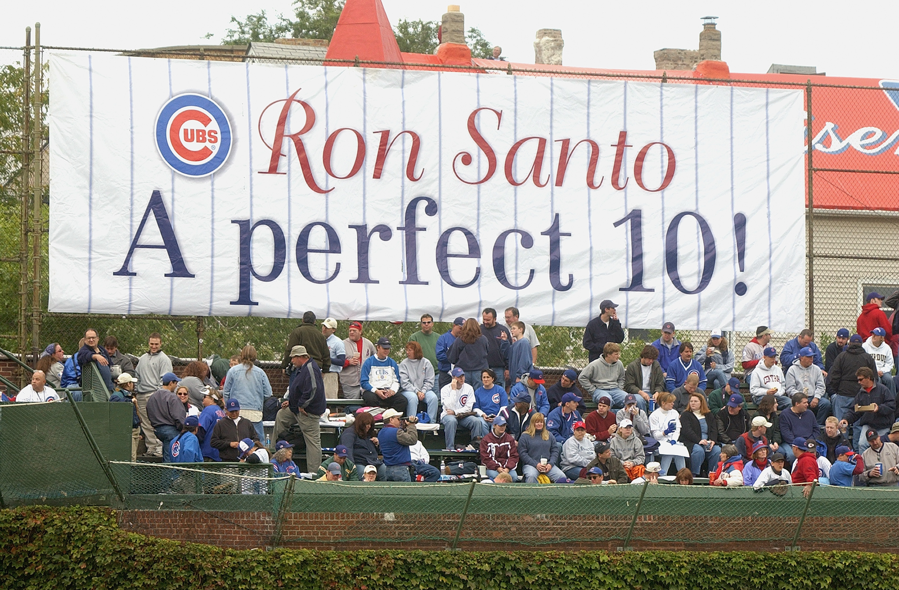 CHICAGO - SEPTEMBER 28:  Fans of the Chicago Cubs watch the game in front of a sign honoring longtime Cubs third baseman and current WGN Radio color commentator Ron Santo (Santo's number 10 was retired in a pregame ceremony) during a game against the Pitt