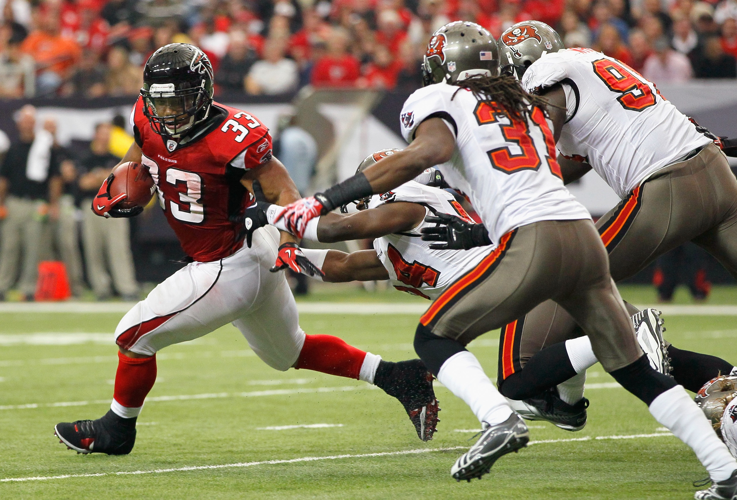 ATLANTA - NOVEMBER 07:  Michael Turner #33 of the Atlanta Falcons rushes away from Geno Hayes #54, E.J. Biggers #31 and Stylez G. White #91 of the Tampa Bay Buccaneers at Georgia Dome on November 7, 2010 in Atlanta, Georgia.  (Photo by Kevin C. Cox/Getty 