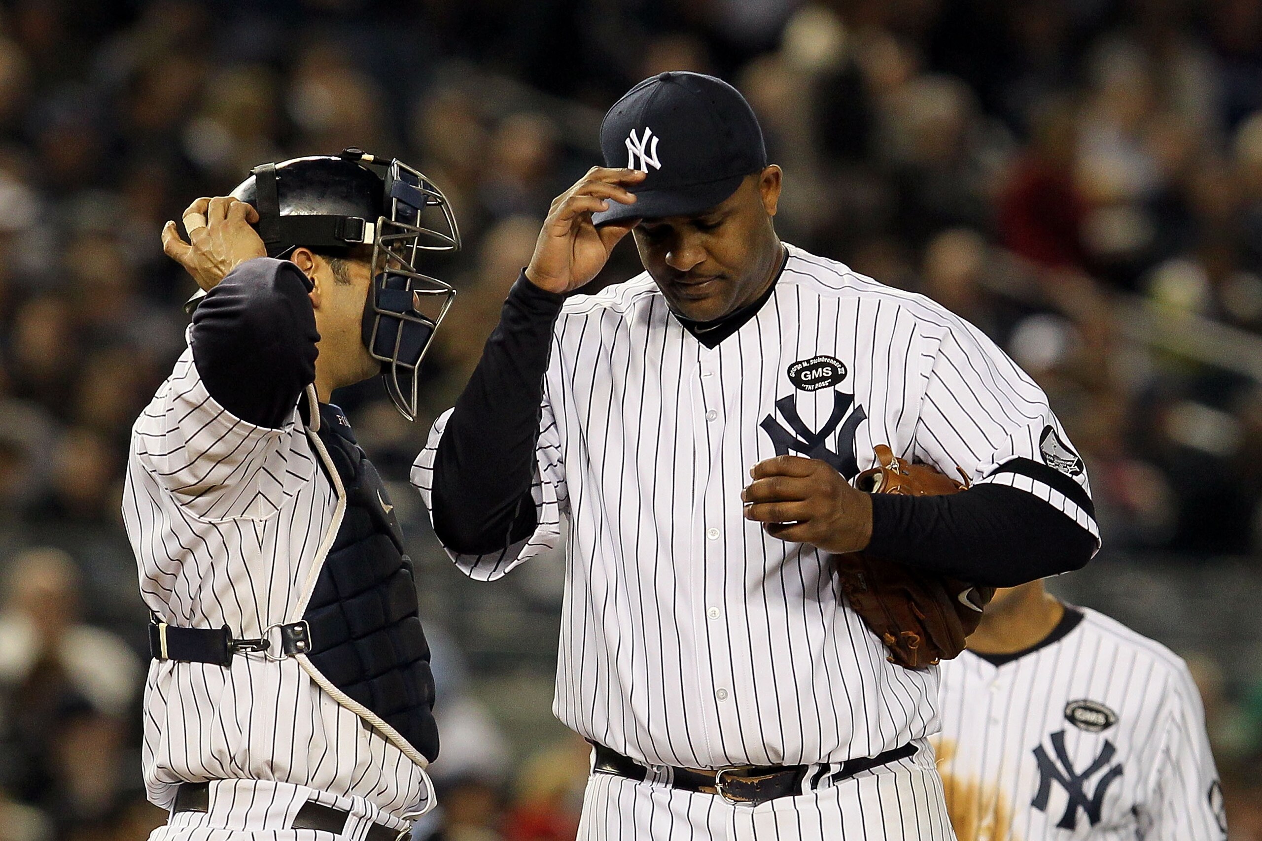 NEW YORK - OCTOBER 20:  Starting pitcher CC Sabathia #52 of the New York Yankees adjusts his cap as he talks with catcher Jorge Posada #20 after Sabathia gave up a single to Jeff Francoeur #21 of the Texas Rangers to load the bases in the top of the sixth