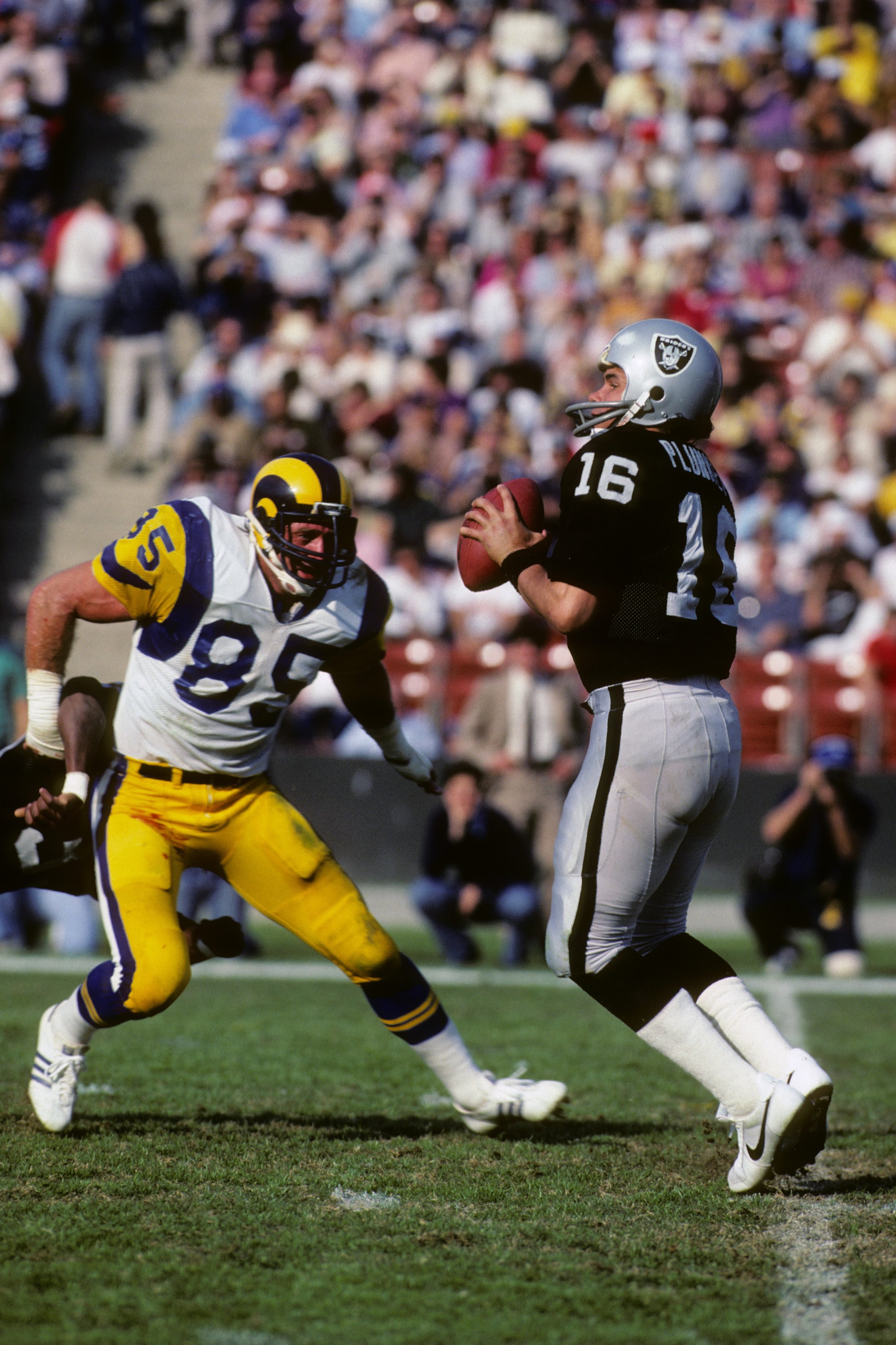 LOS ANGELES - DECEMBER 18:  Quarterback Jim Plunkett #16 of the Los Angeles Raiders drops back to pass against defensive end Jack Youngblood #85 of the Los Angeles Rams during the game at the Los Angeles Memorial Coliseum on December 18, 1982 in Los Angel