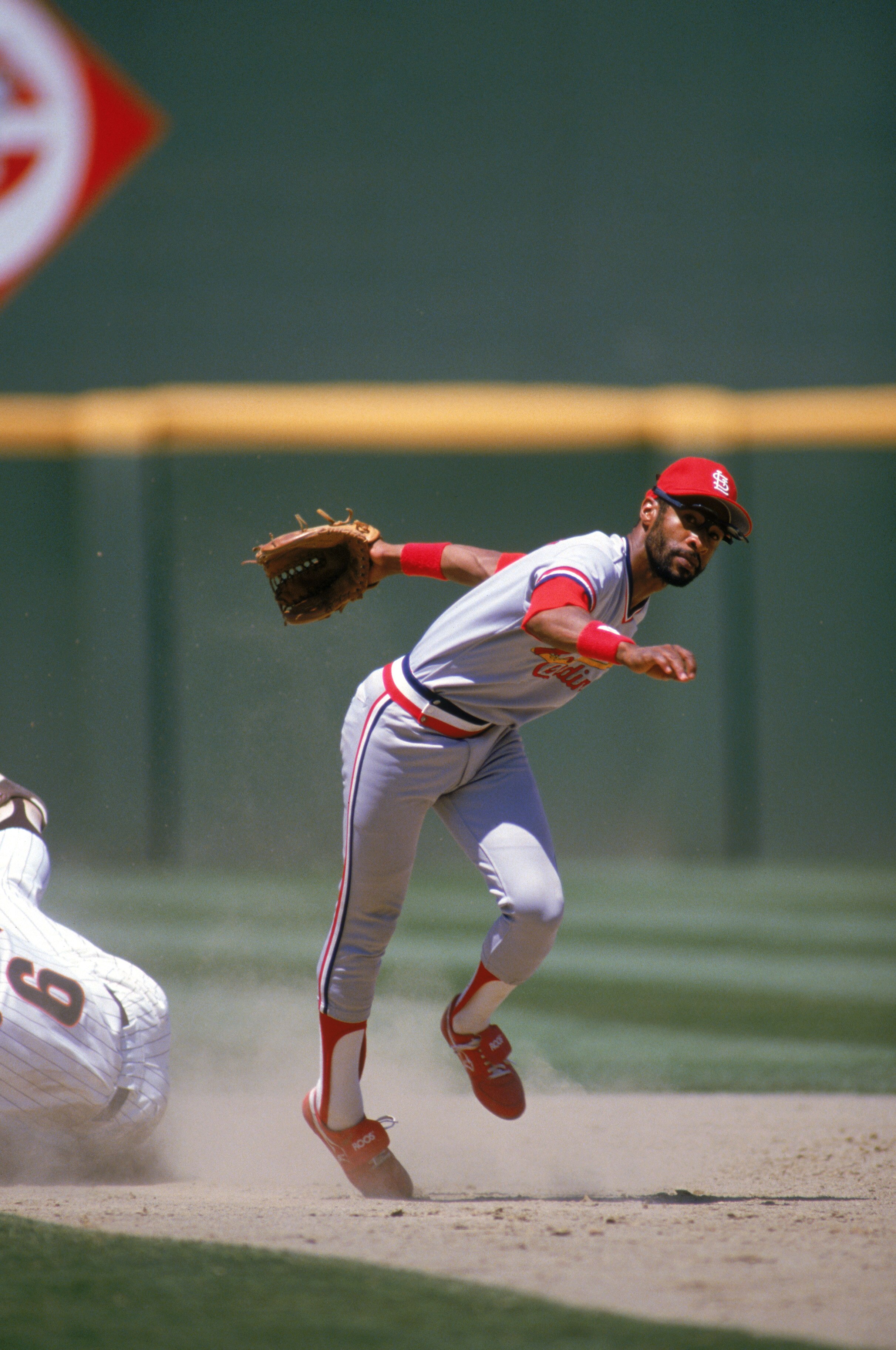SAN DIEGO - 1985:  Ozzie Smith #1 of the St. Louis Cardinals stumbles after dodging a sliding San Diego Padres base runner during a game in 1985 at Jack Murphy Stadium in San Diego, California.  (Photo by Stephen Dunn/Getty Images)