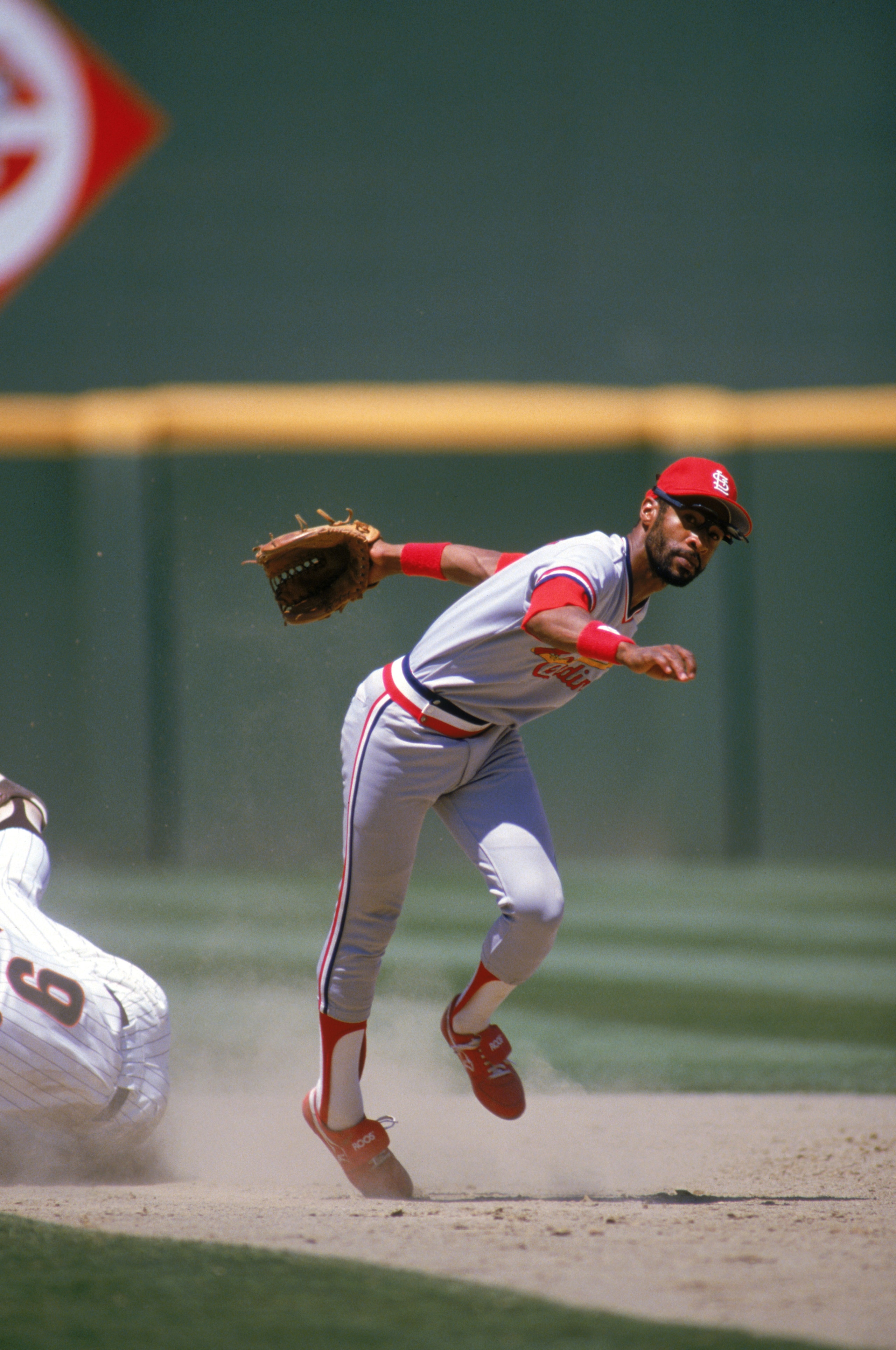 SAN DIEGO - 1985:  Ozzie Smith #1 of the St. Louis Cardinals stumbles after dodging a sliding San Diego Padres base runner during a game in 1985 at Jack Murphy Stadium in San Diego, California.  (Photo by Stephen Dunn/Getty Images)