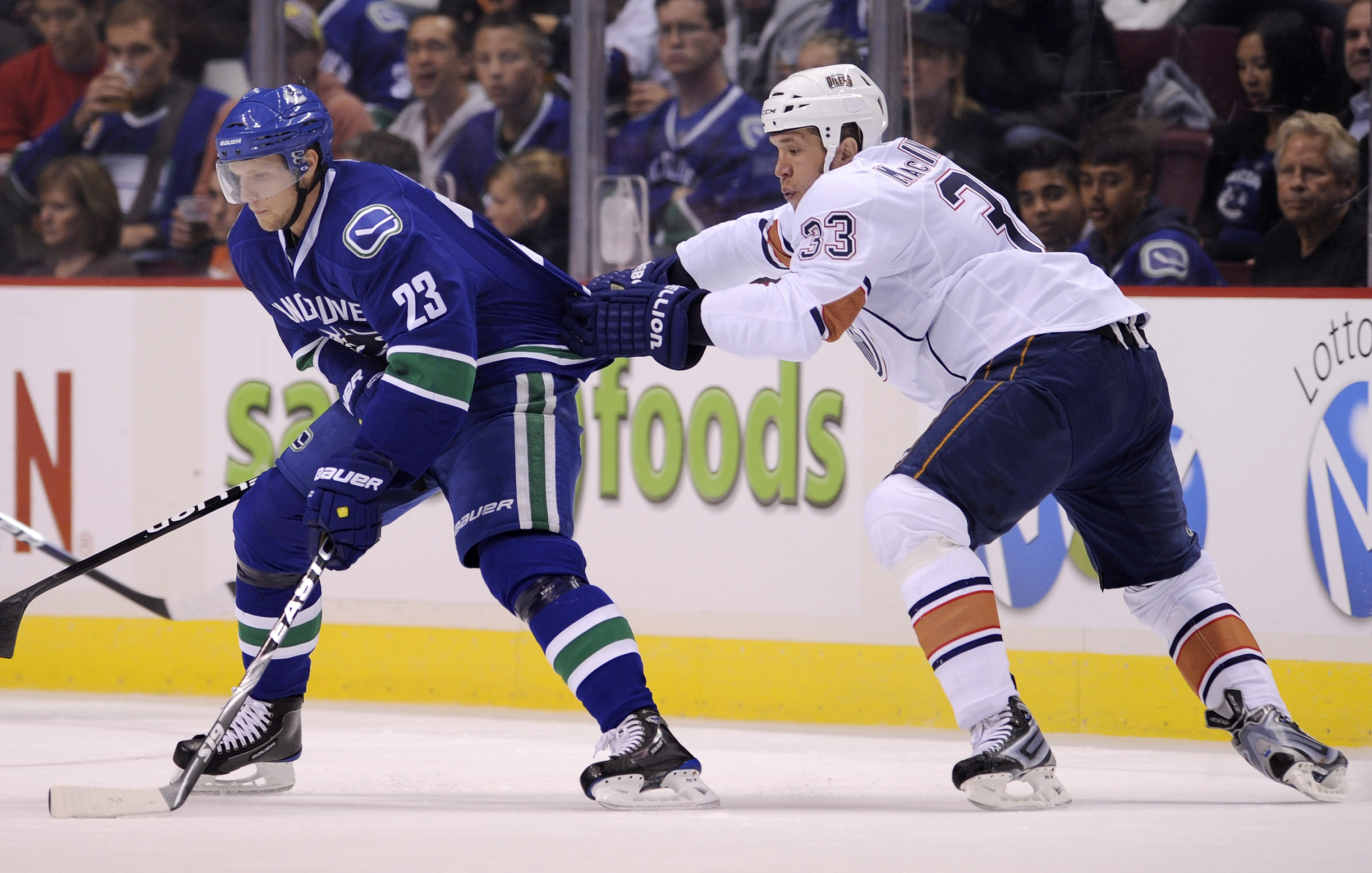 VANCOUVER, CANADA - SEPTEMBER 22: Steve MacIntyre #33 of the Edmonton Oilers grabs a hold of Alex Edler's #23 of the Vancouver Canucks jersey during the second period in preseason NHL action on September 22, 2010 at Rogers Arena in Vancouver, British Colu