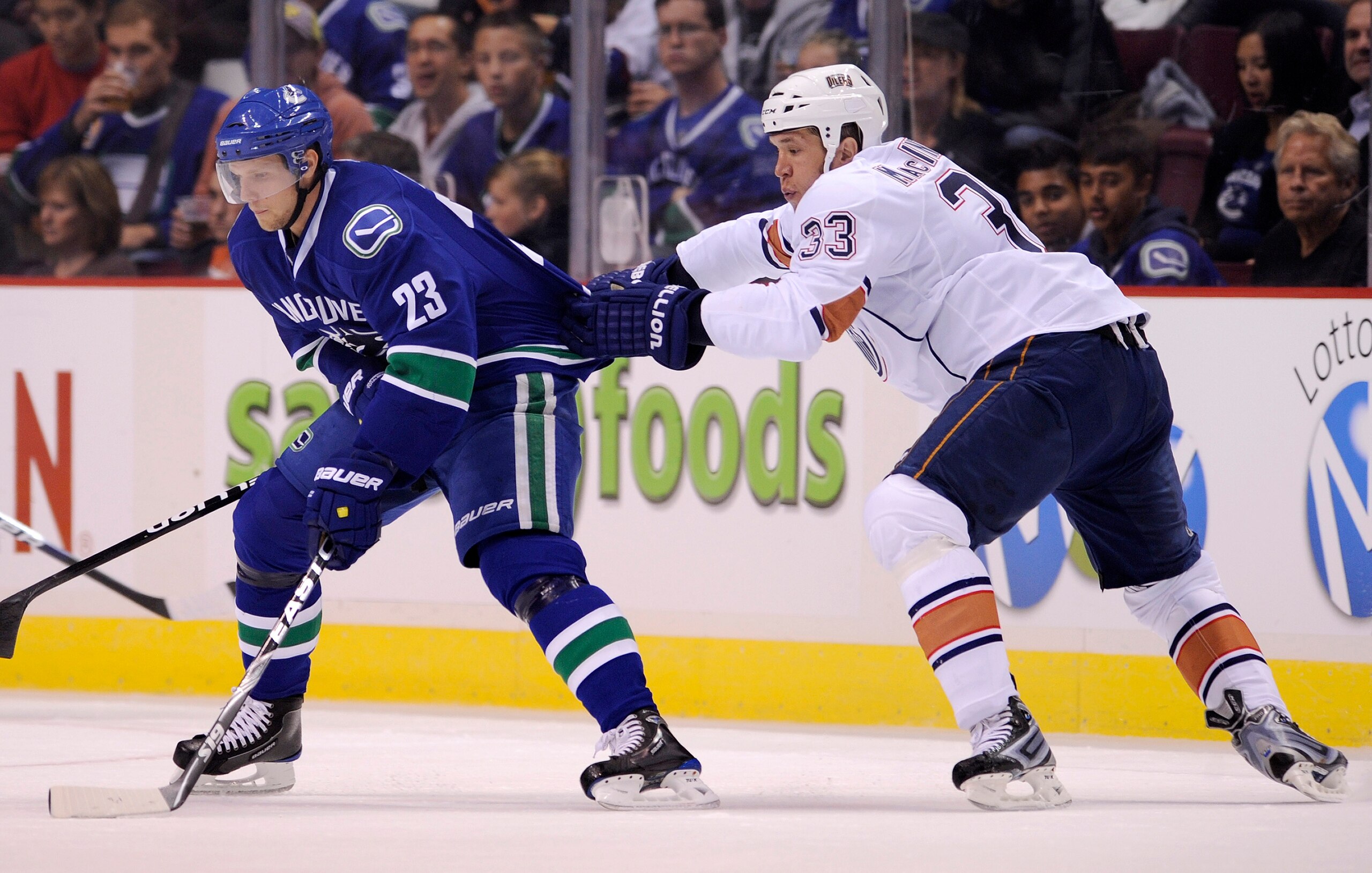 VANCOUVER, CANADA - SEPTEMBER 22: Steve MacIntyre #33 of the Edmonton Oilers grabs a hold of Alex Edler's #23 of the Vancouver Canucks jersey during the second period in preseason NHL action on September 22, 2010 at Rogers Arena in Vancouver, British Colu