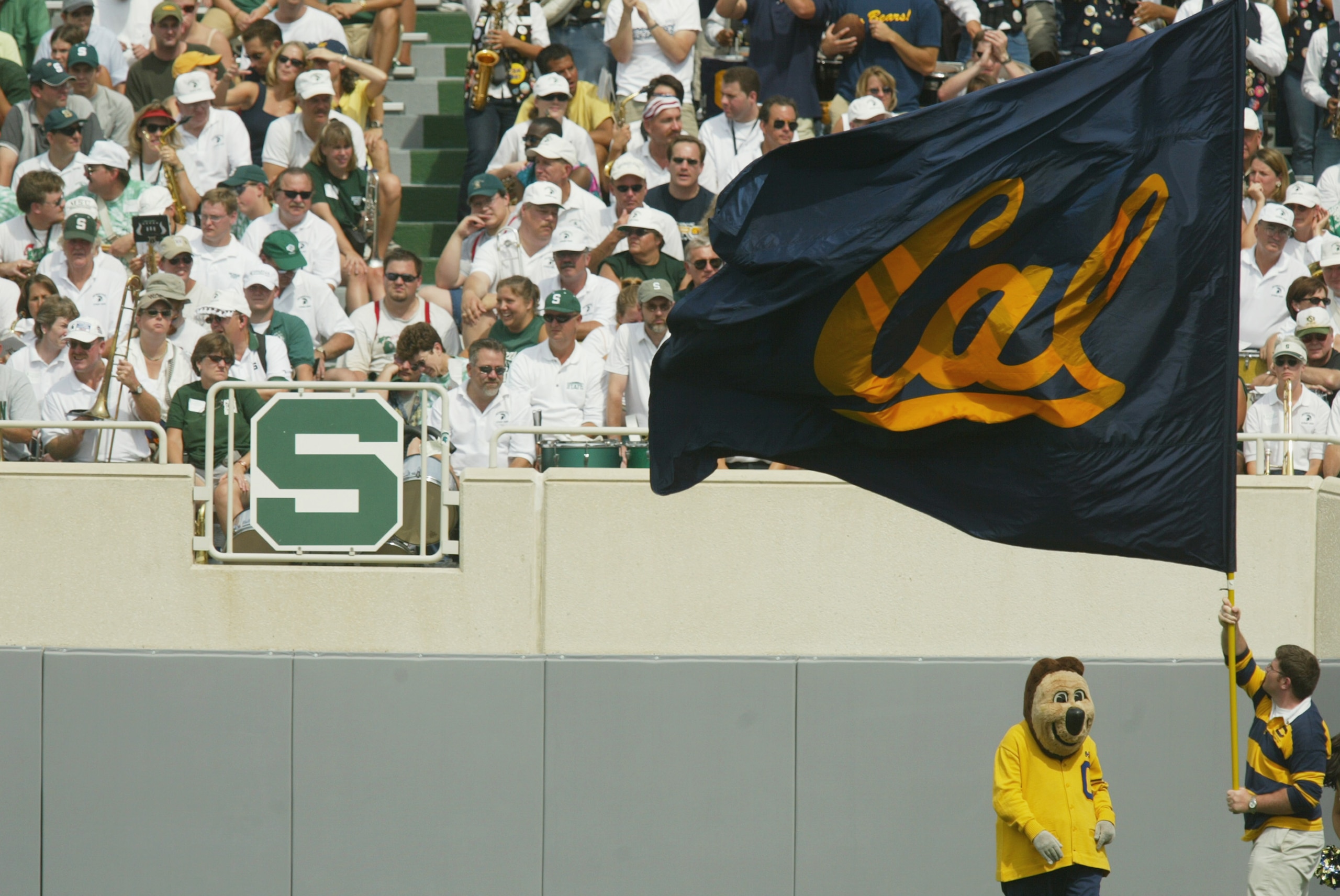 EAST LANSING, MI - SEPTEMBER 14: A member of the California Golden Bears spirit squad waves a team flag while standing next to the Bears' mascot in front of the Michigan State Spartans crowd on September 14, 2002 at Spartan Stadium in East Lansing, Michi EAST LANSING, MI - SEPTEMBER 14: A member of the California Golden Bears spirit squad waves a team flag while standing next to the Bears' mascot in front of the Michigan State Spartans crowd on September 14, 2002 at Spartan Stadium in East Lansing, Michi