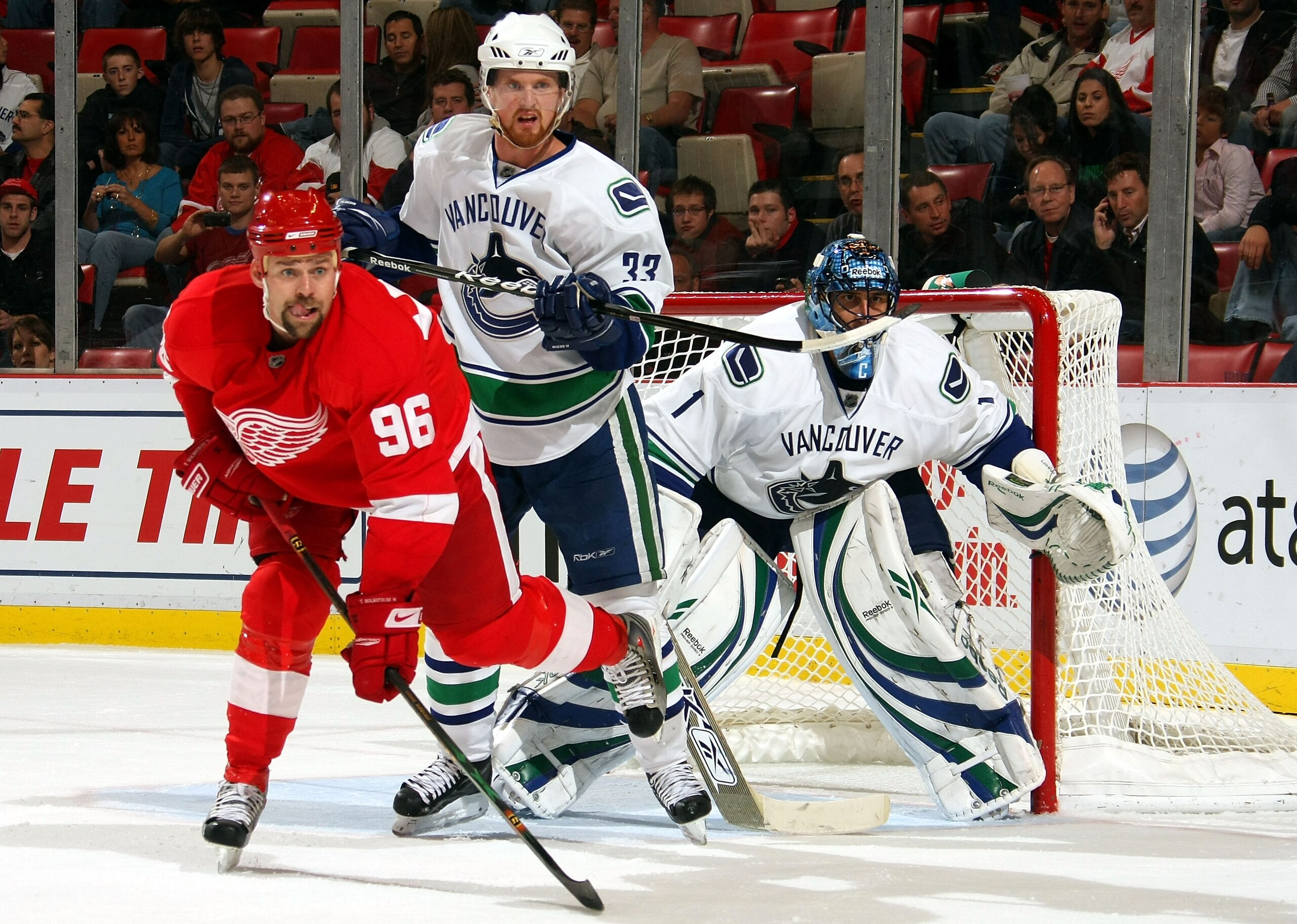 DETROIT - OCTOBER 16:  Tomas Holmstrom #96 of the Detroit Red Wings battles for position with Henrik Sedin #33 of the Vancouver Canucks as Roberto Luongo #1 of the Vancouver Canucks keeps an eye on the play during their NHL game at Joe Louis Arena October
