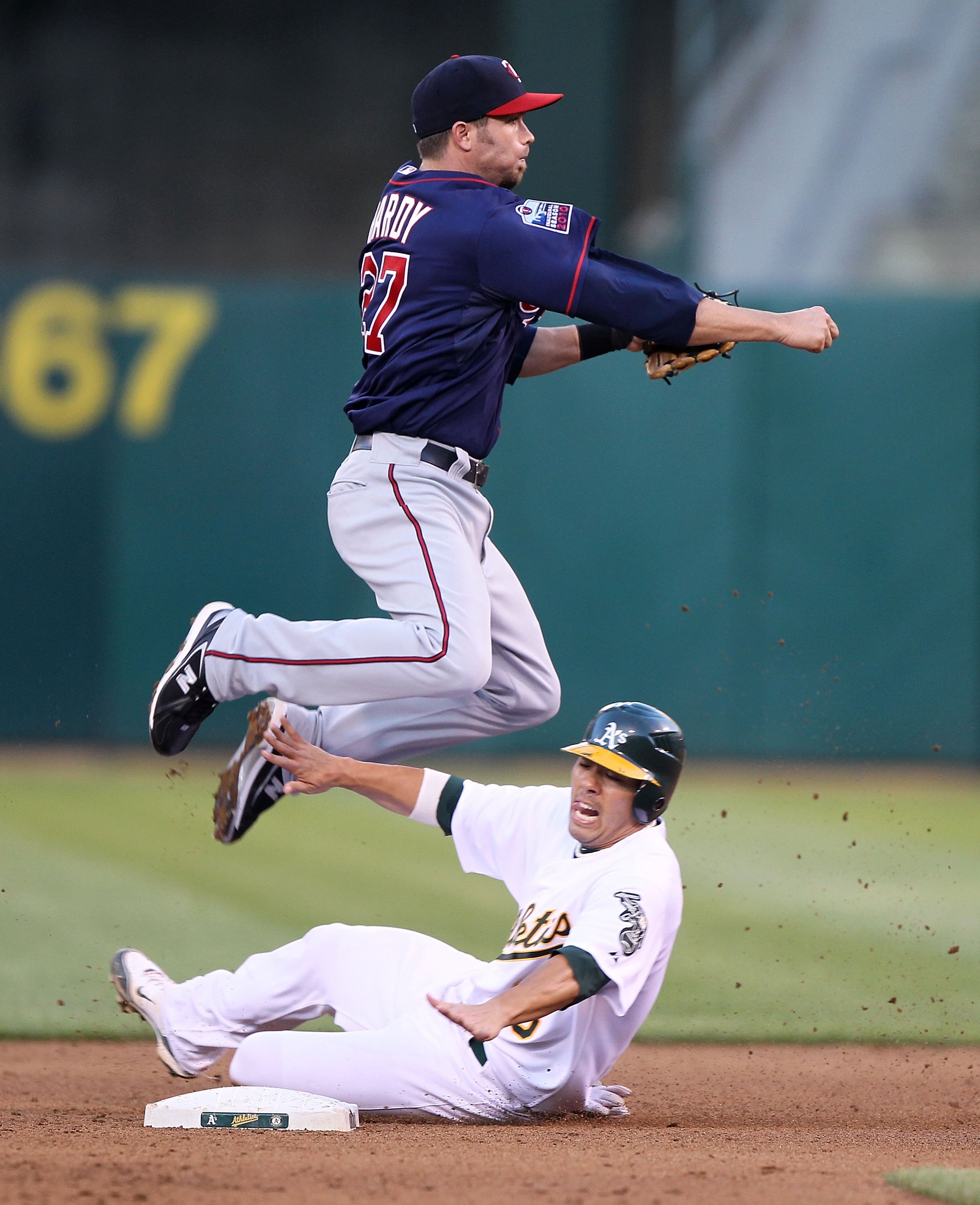 OAKLAND, CA - JUNE 04:  J.J. Hardy #27 of the Minnesota Twins leaps over Kurt Suzuki #8 of the Oakland Athletics on a double play hit by Jack Cust in the fourth inning during an MLB game at the Oakland-Alameda County Coliseum on June 4, 2010 in Oakland, C