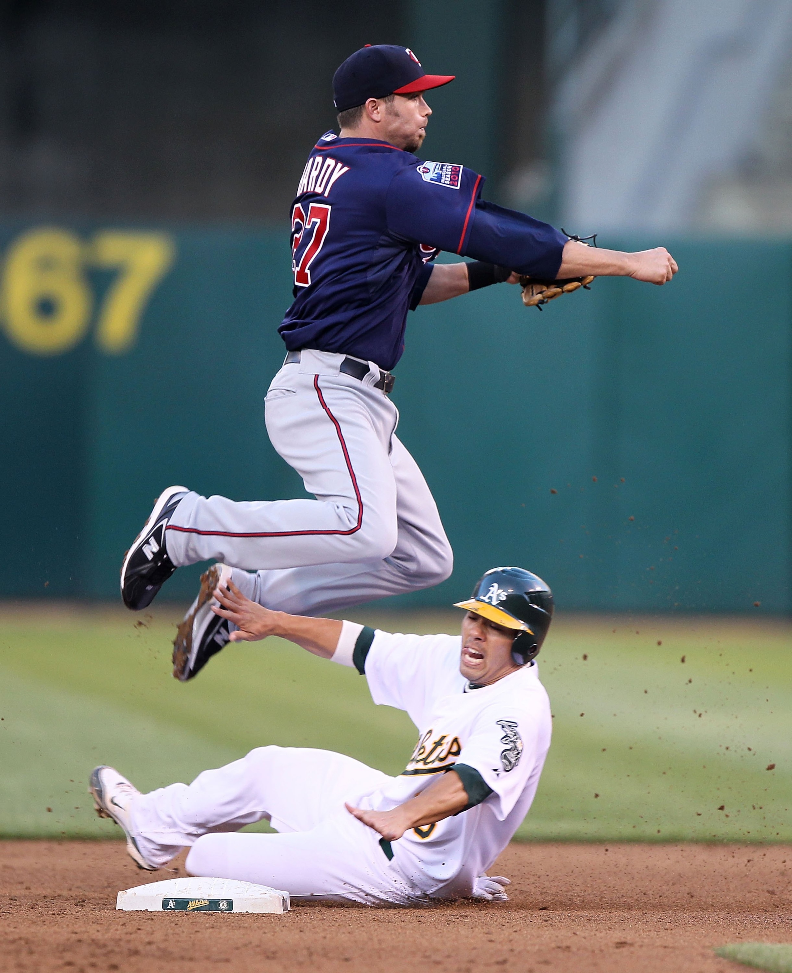 OAKLAND, CA - JUNE 04:  J.J. Hardy #27 of the Minnesota Twins leaps over Kurt Suzuki #8 of the Oakland Athletics on a double play hit by Jack Cust in the fourth inning during an MLB game at the Oakland-Alameda County Coliseum on June 4, 2010 in Oakland, C