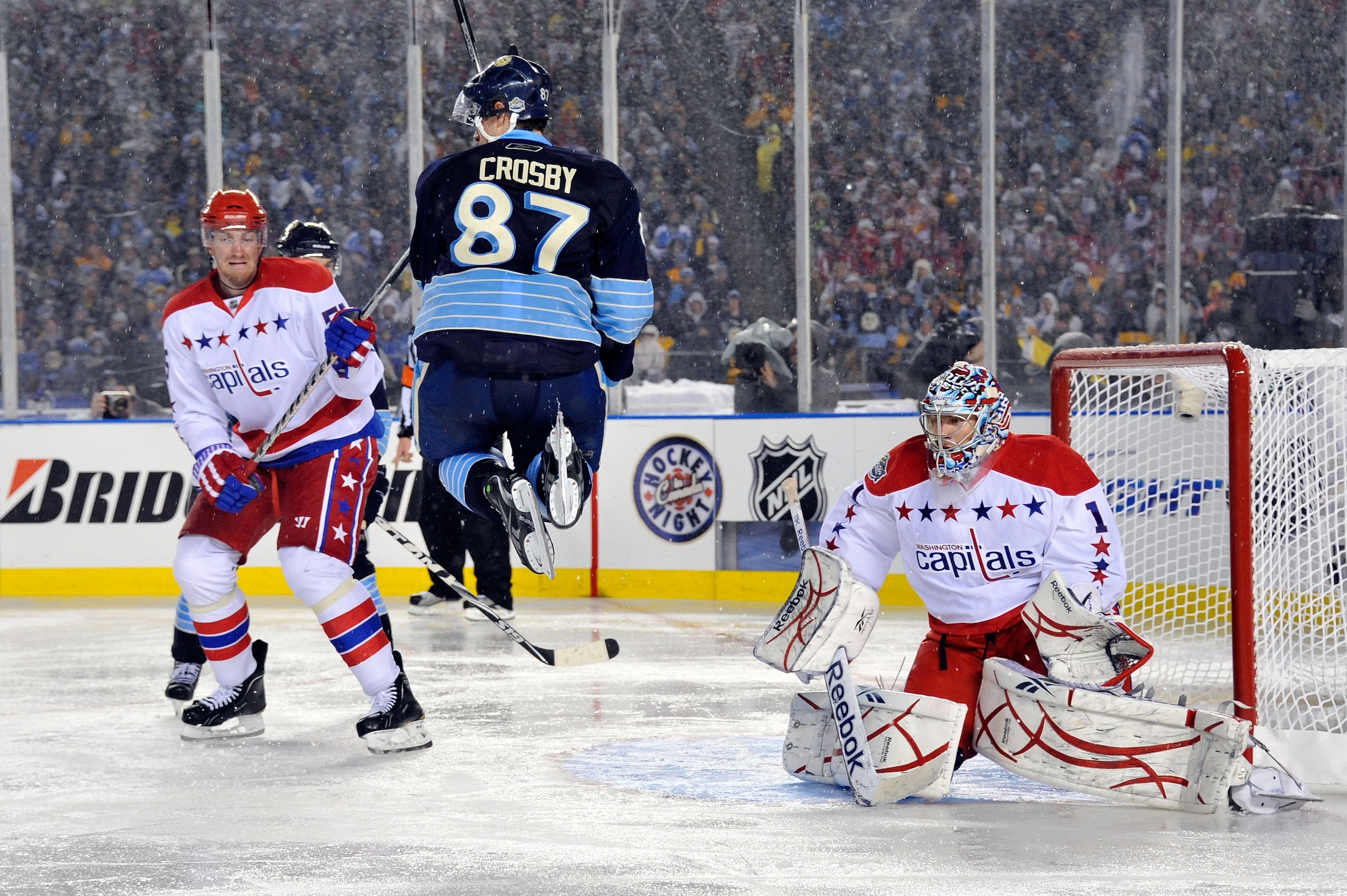 PITTSBURGH, PA - JANUARY 01:  Sidney Crosby #87 of the Pittsburgh Penguins jumps to get out of the way as Semyon Varlamov #1 of the Washington Capitals defends the net during the 2011 NHL Bridgestone Winter Classic at Heinz Field on January 1, 2011 in Pit